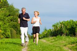 A Caucasian man and woman running through a wooded trail.