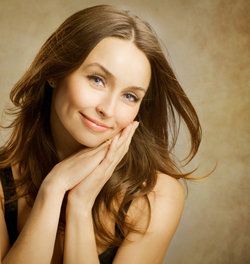 Attractive brunette smiling and clasping hands to cheek